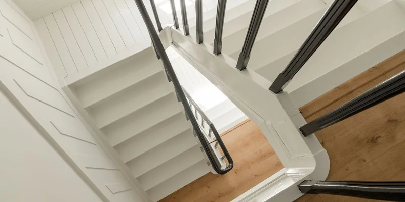 An indoor staircase with contrasting step nosings, a handrail and bright overhead light.