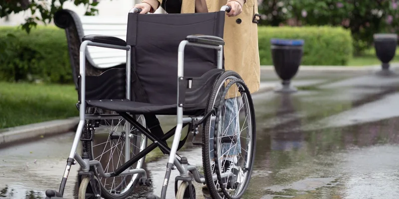 A lightweight transport chair with small rear wheels opened out in a hallway.