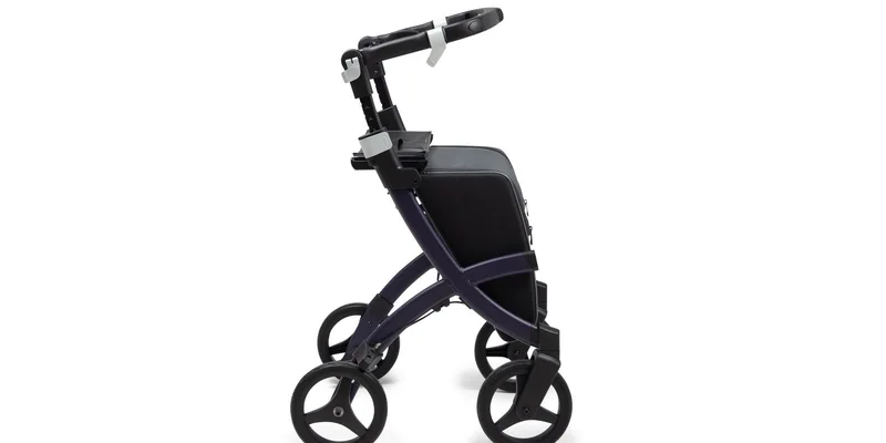 An upright rollator with padded forearm platforms standing in a bright hallway.