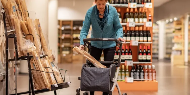 An older woman pushes a rollator through a shop.